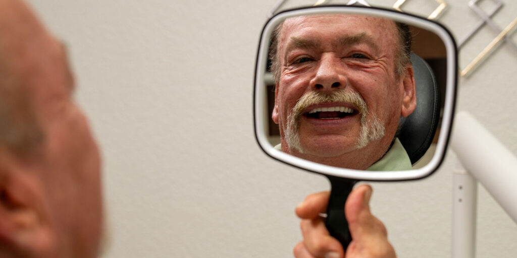 Paitent looking into mirror at their new teeth